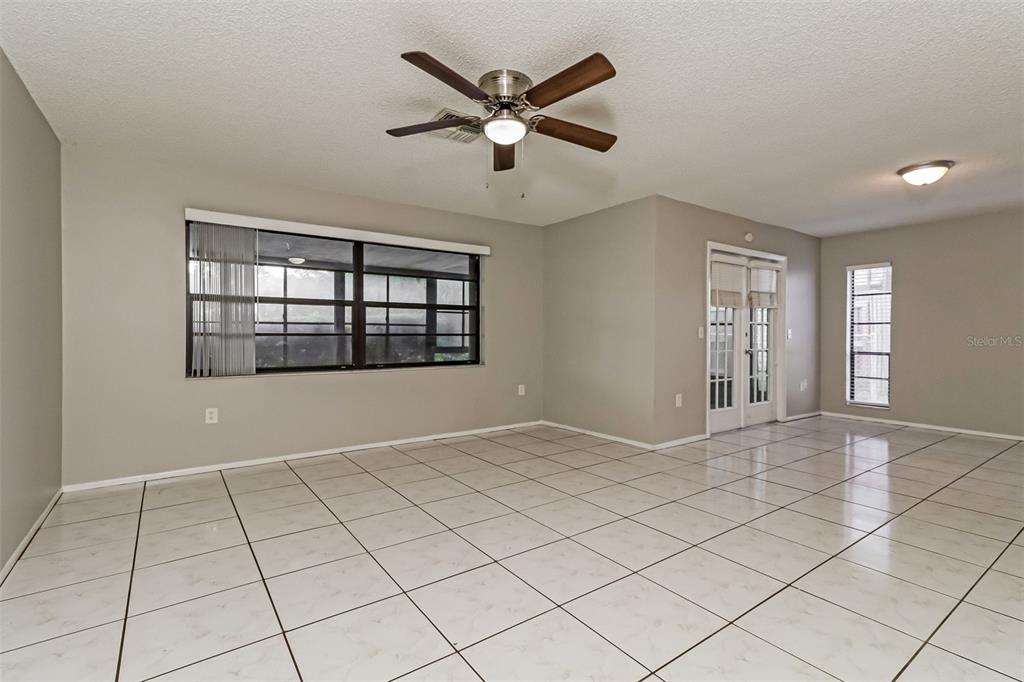 An empty room with light-colored tile flooring, a ceiling fan, and large windows — 11322 WOLF COURT, PORT RICHEY, FL