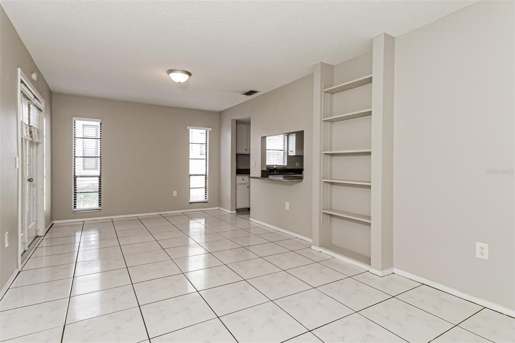 A dining area with white tile floors, built-in shelving, and a pass-through to the kitchen — 11322 WOLF COURT, PORT RICHEY, FL