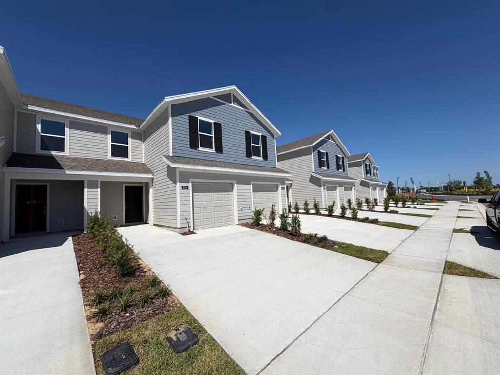 A row of modern townhomes features light gray siding, blue accents, and concrete driveways — 836 LYNX STREET, DAVENPORT, FL