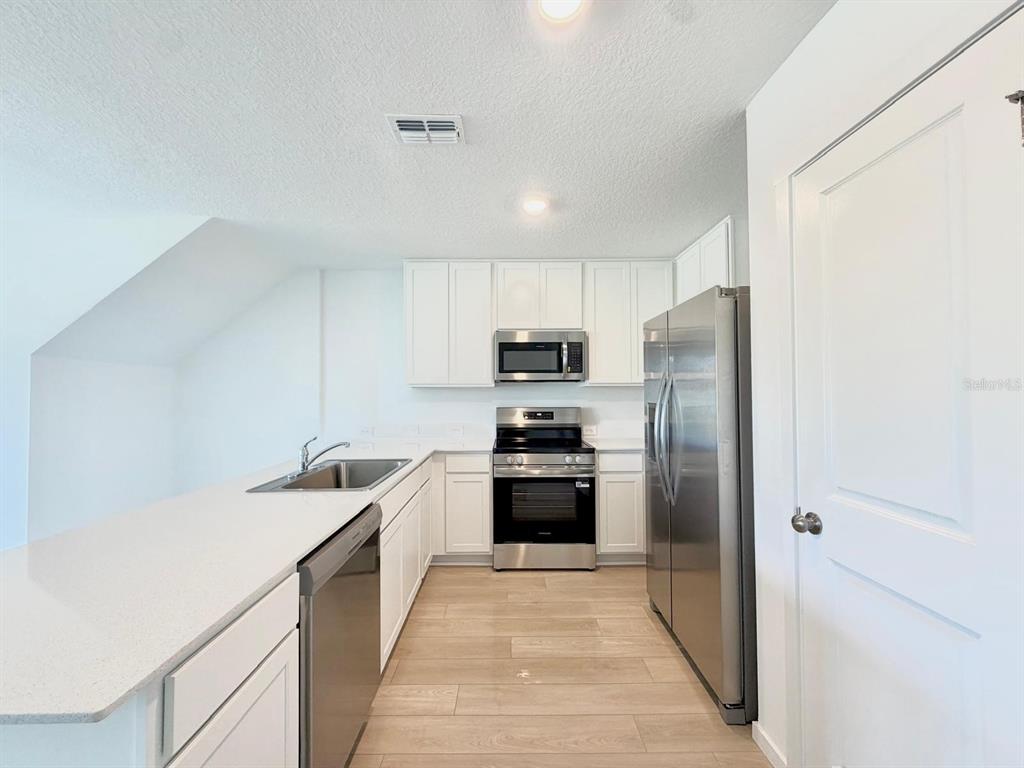 A kitchen features white cabinets, stainless steel appliances, and a light-colored countertop — 836 LYNX STREET, DAVENPORT, FL