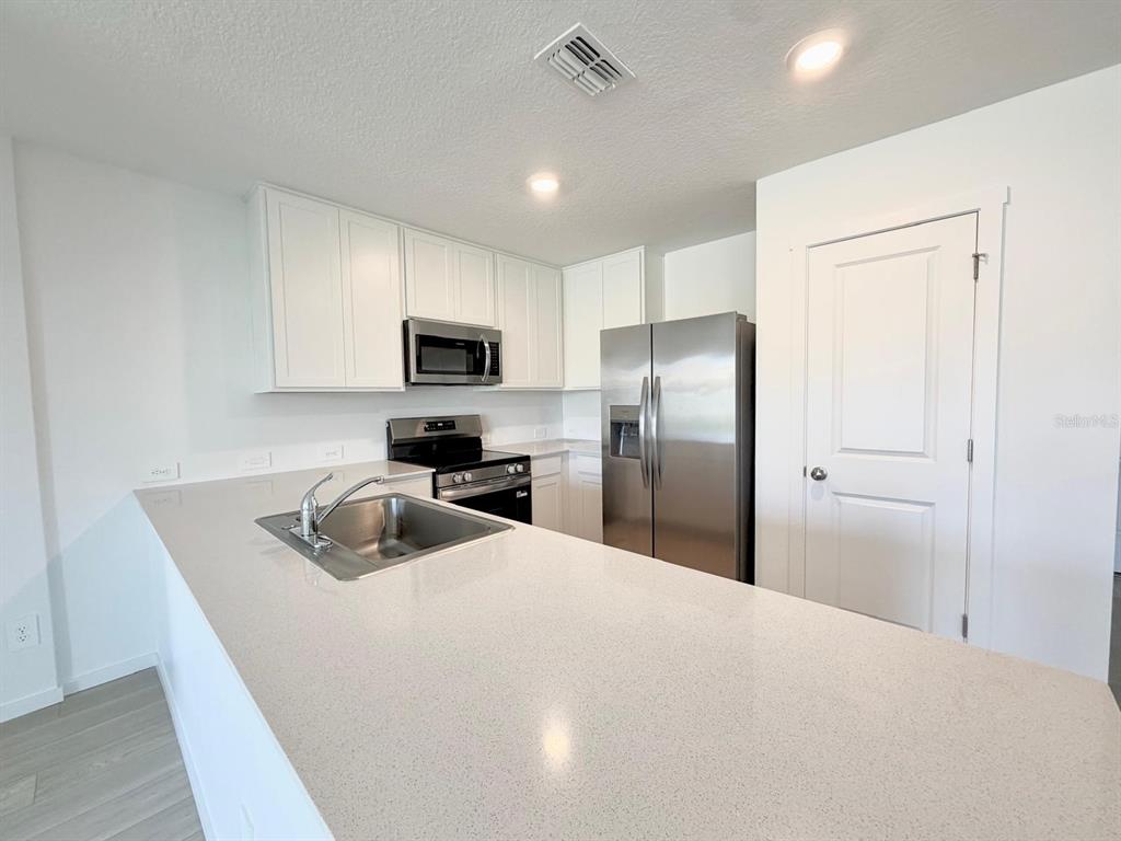 A kitchen features white cabinets, stainless steel appliances, and a light-colored quartz countertop island — 836 LYNX STREET, DAVENPORT, FL