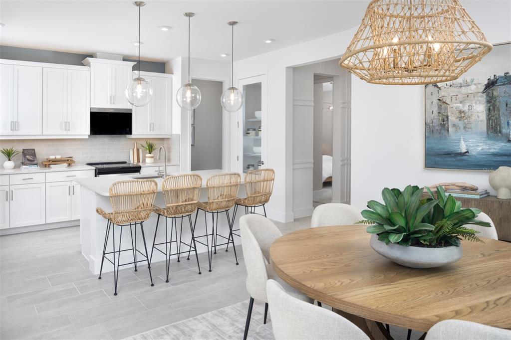 A modern kitchen with white cabinets, a central island, and a dining area with rattan chairs — 11740 BOUNDLESS TERRACE, VENICE, FL