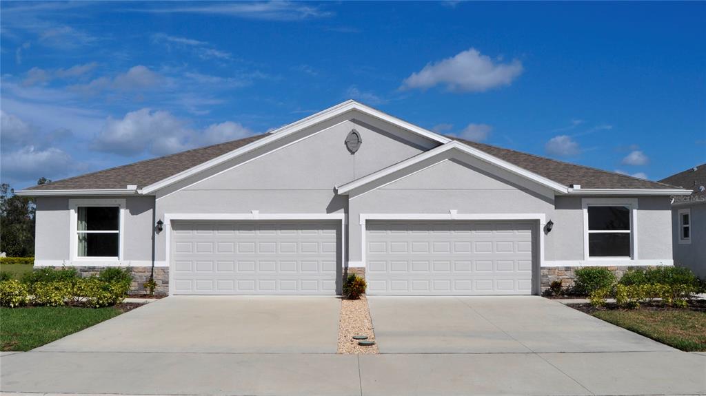 A single-story duplex with two garage doors, light gray stucco, and stone accents — 18350 TAVERNSIDE TRAIL, LAKEWOOD RANCH, FL