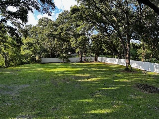A grassy, tree-filled backyard is enclosed by a white vinyl fence — 17430 BLACKWELL LANE, LUTZ, FL