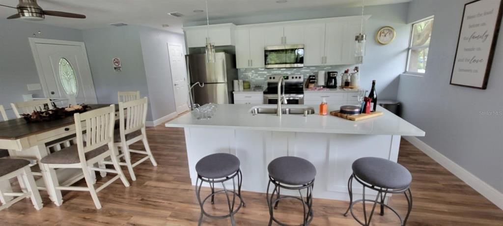 A kitchen features a white island with bar stools, stainless steel appliances, and wood flooring — 17430 BLACKWELL LANE, LUTZ, FL