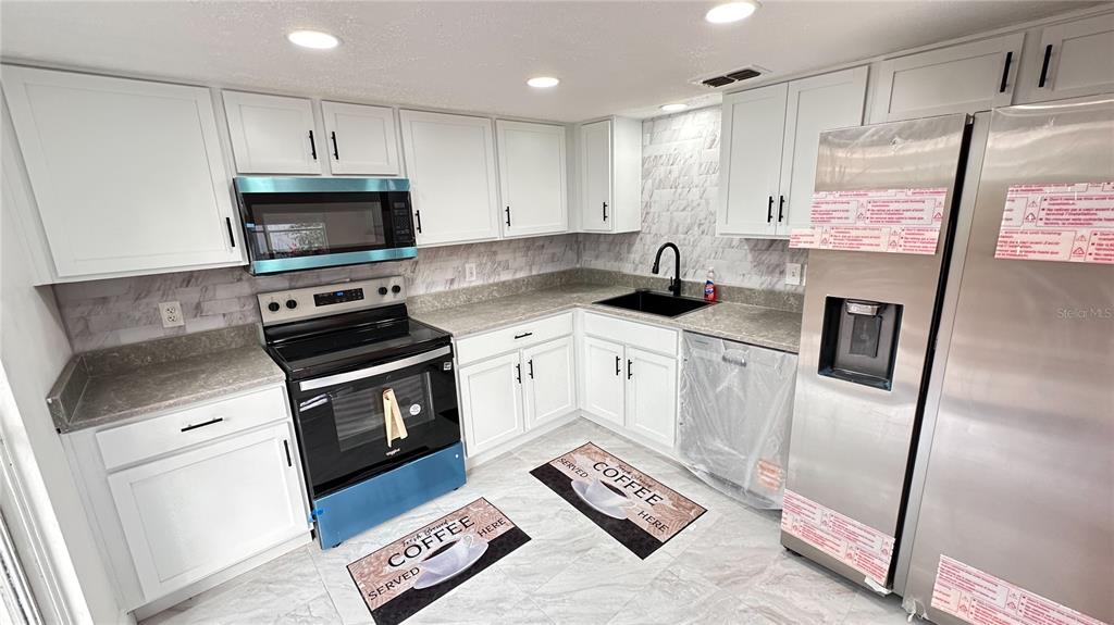 An empty room with wood-look flooring, a staircase with a gray railing, and two windows — 2320 PEBBLE BROOK ROAD, KISSIMMEE, FL
