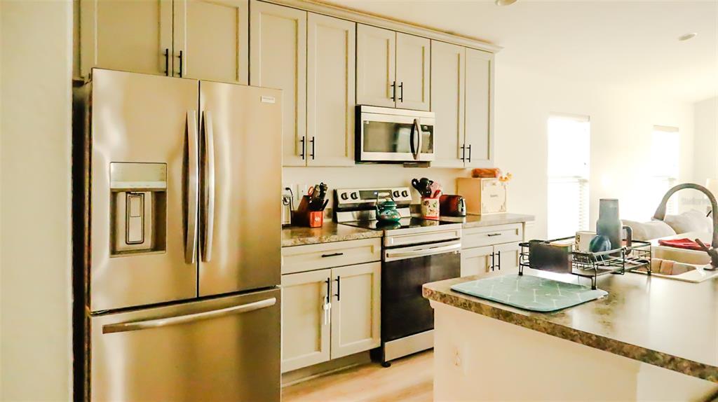 A kitchen features light-colored cabinets, stainless steel appliances, and a central island with a sink — 1317 KESTREL COURT, AVON PARK, FL