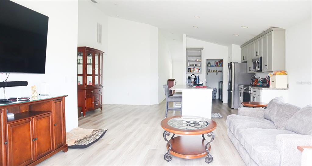 An open-concept living room and kitchen area features light wood flooring and gray cabinetry — 1317 KESTREL COURT, AVON PARK, FL