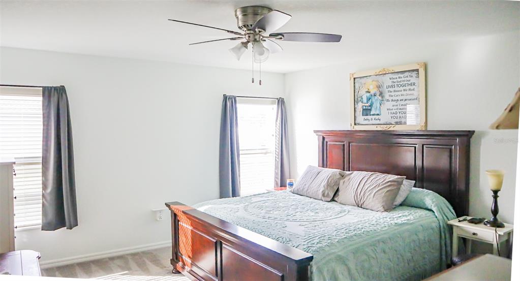 A bedroom features a dark wood bed frame, a ceiling fan, and two windows with curtains — 1317 KESTREL COURT, AVON PARK, FL