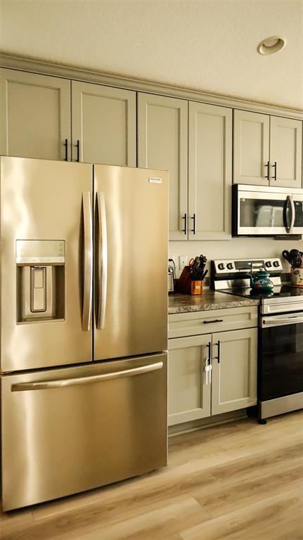 A kitchen features light gray cabinets, stainless steel appliances, and wood-look flooring — 1317 KESTREL COURT, AVON PARK, FL