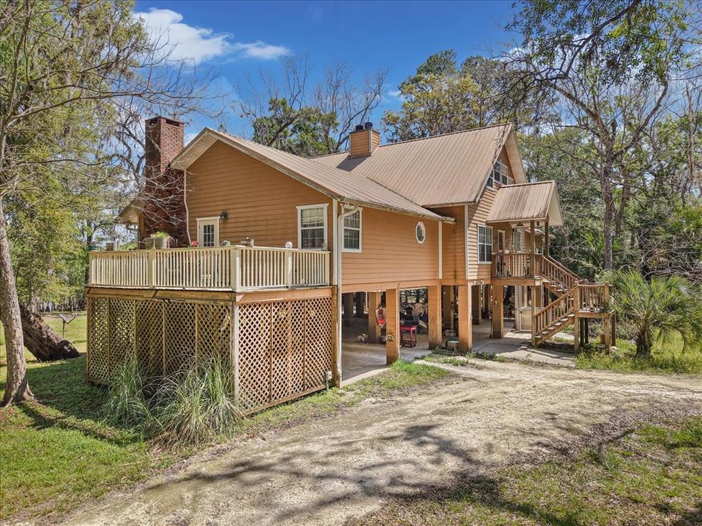 A two-story house with tan siding, a metal roof, and an elevated deck on stilts — 124 NE 824TH STREET, OLD TOWN, FL