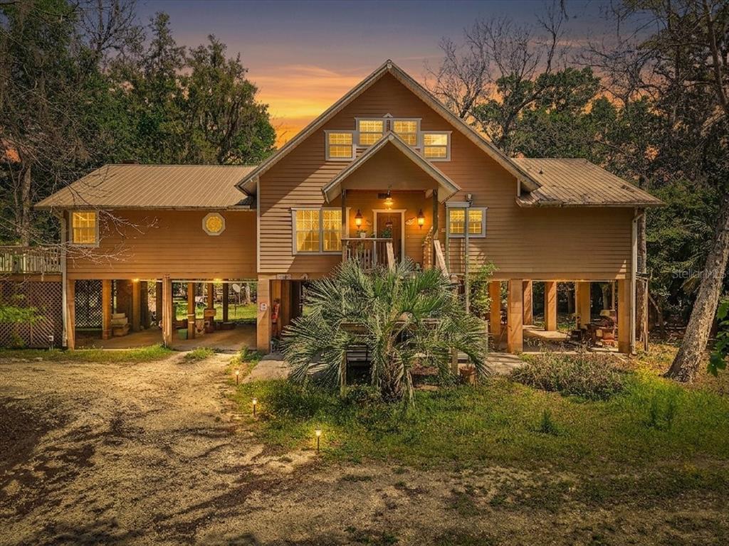 A stilt house with tan siding and a metal roof stands above a gravel driveway — 124 NE 824TH STREET, OLD TOWN, FL