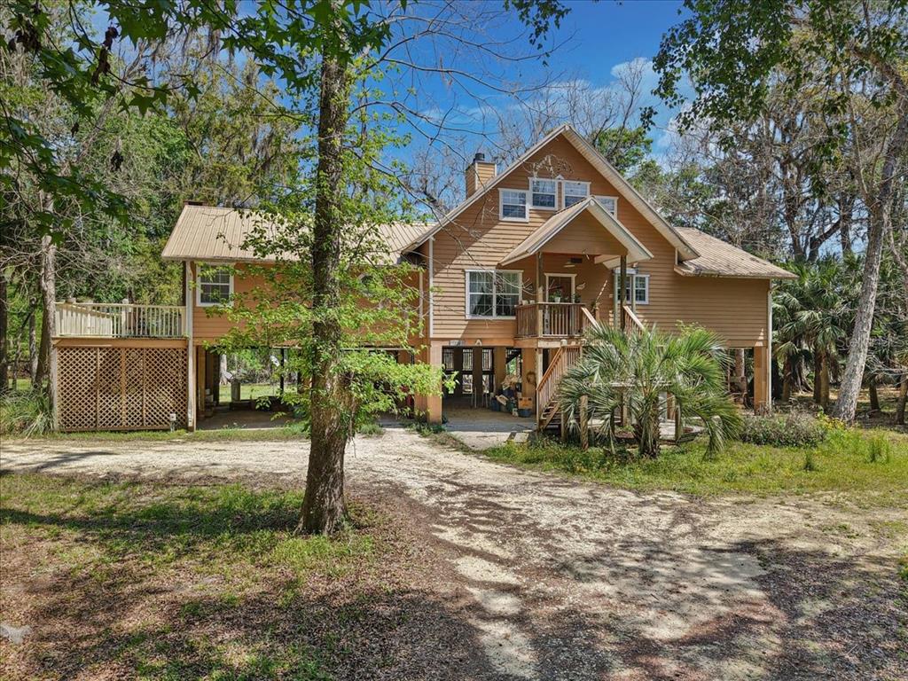 A two-story stilt house with tan siding and a metal roof sits in a wooded area — 124 NE 824TH STREET, OLD TOWN, FL