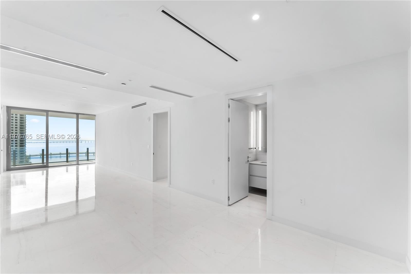 A bright, minimalist room features white marble floors, recessed lighting, and a view of water — 300 Biscyane Blvd Way # 1202, Miami FL 33131, MIAMI, FL