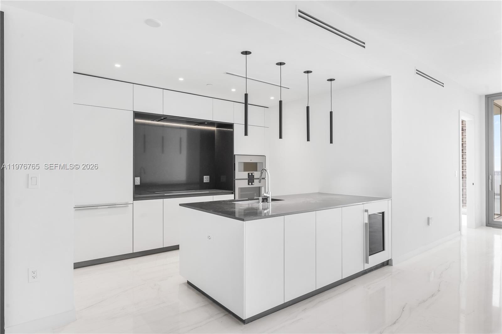A modern kitchen features white cabinetry, a dark stone island, and minimalist pendant lighting — 300 Biscyane Blvd Way # 1202, Miami FL 33131, MIAMI, FL