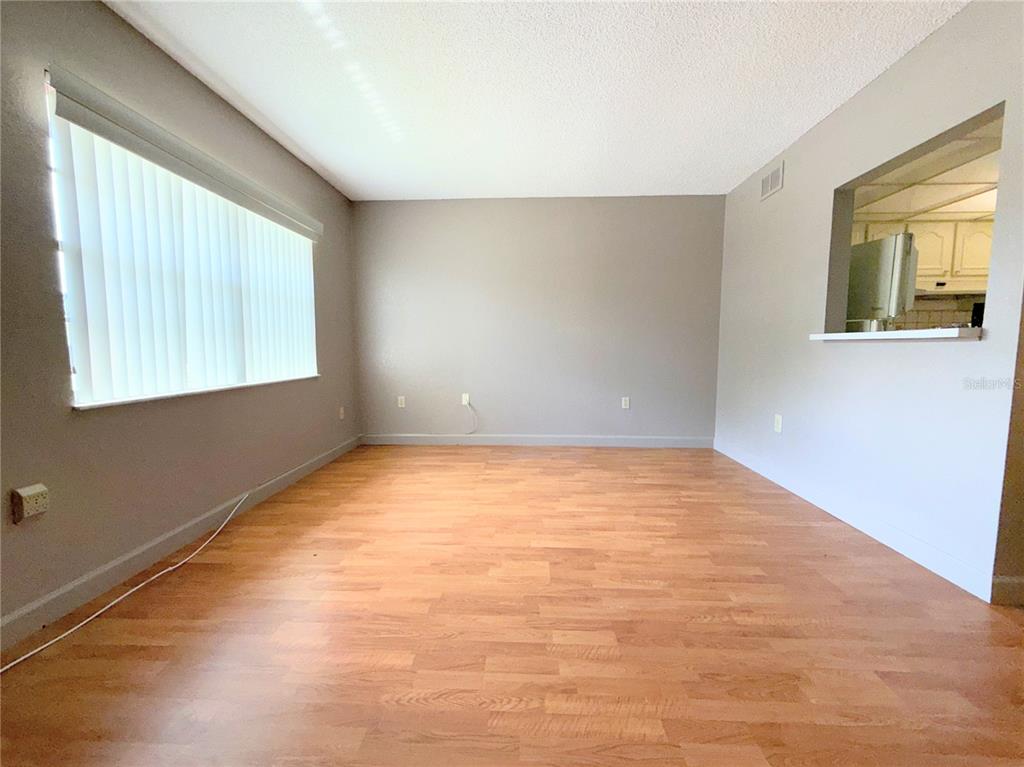 An empty room with light wood-look flooring, gray walls, and a window with vertical blinds — 11931 BAYONET LANE, NEW PORT RICHEY, FL