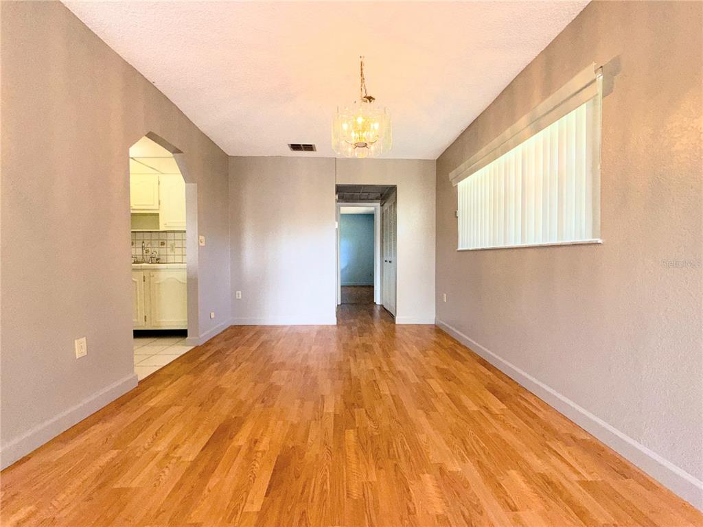 An empty room with hardwood floors, a chandelier, and a view into the kitchen — 11931 BAYONET LANE, NEW PORT RICHEY, FL