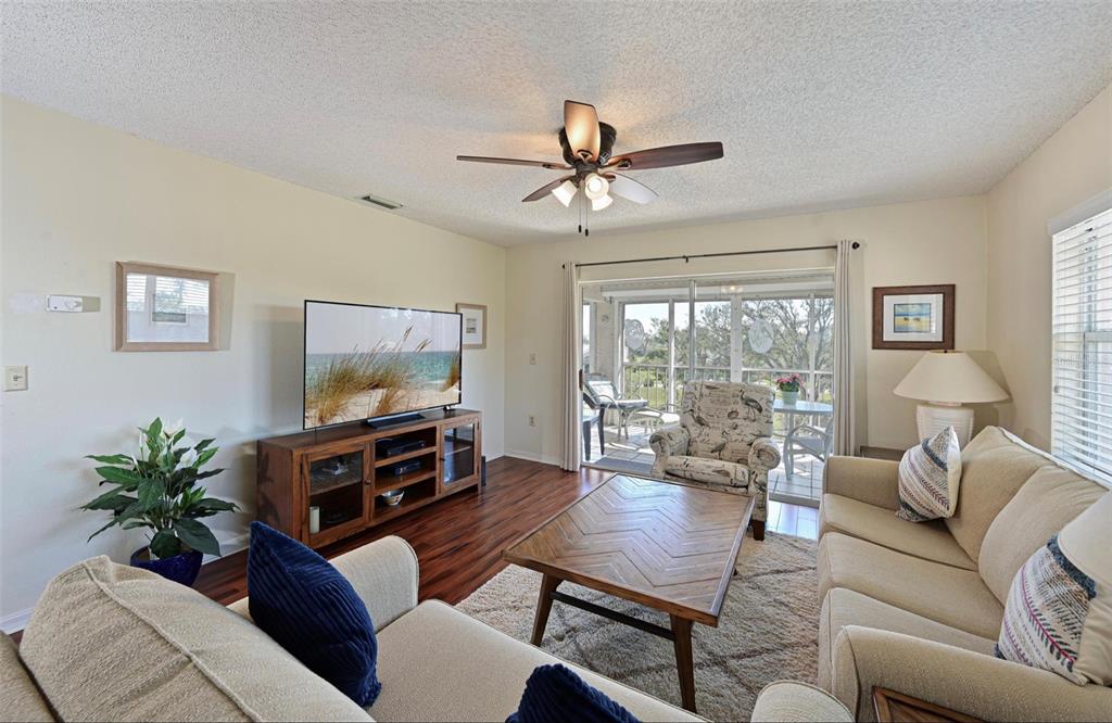 A living room features a ceiling fan, wood flooring, a television console, and sliding glass doors — 6501 STONE RIVER ROAD UNIT 303, BRADENTON, FL
