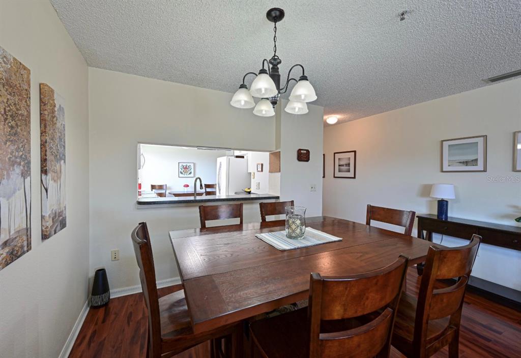 A dining room features a wooden table, chairs, a chandelier, and a kitchen pass-through window — 6501 STONE RIVER ROAD UNIT 303, BRADENTON, FL