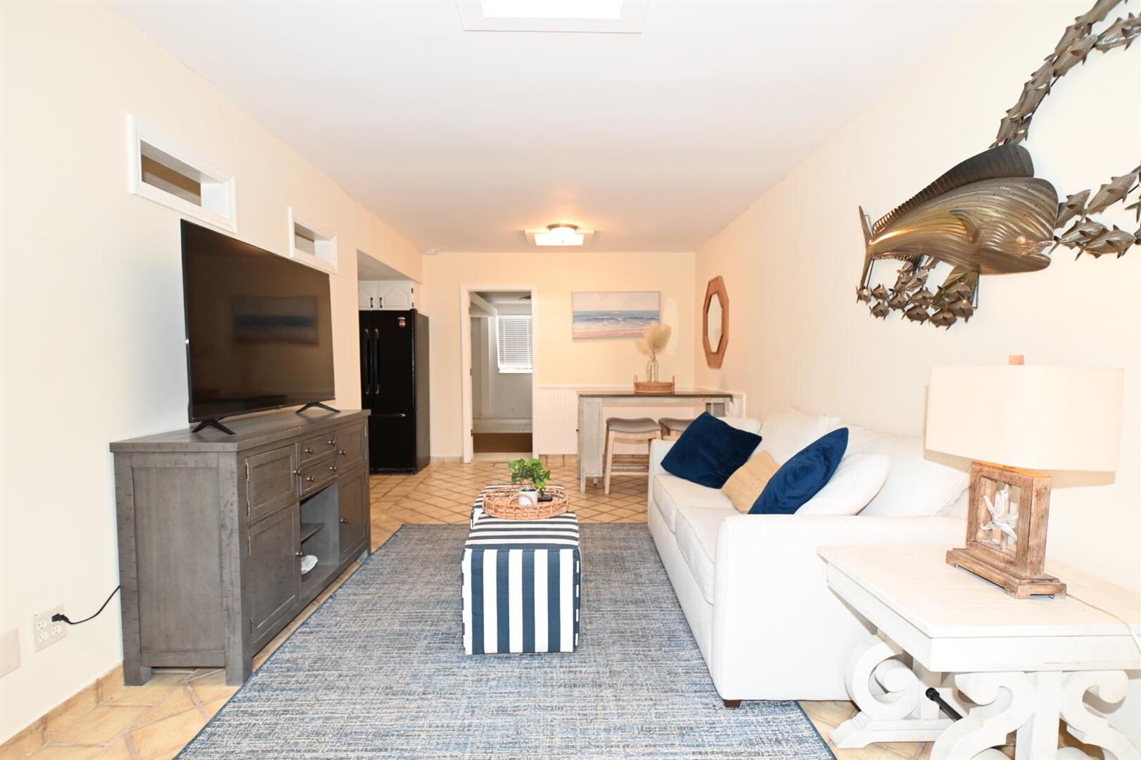 A living room features a white sofa, blue striped ottoman, television console, and wall art — 701 W Ocean Avenue, Boynton Beach FL 33426, BOYNTON BEACH, FL