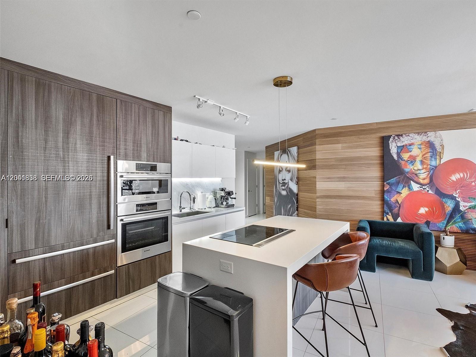 A modern kitchen features wood-paneled cabinetry, a central island with bar seating, and colorful artwork — 851 NE 1st Ave # 4109, Miami FL 33132, MIAMI, FL