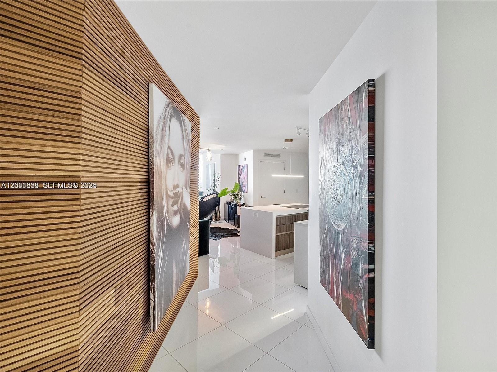 A hallway with wood-slatted walls and artwork leads into a modern kitchen with white floors — 851 NE 1st Ave # 4109, Miami FL 33132, MIAMI, FL