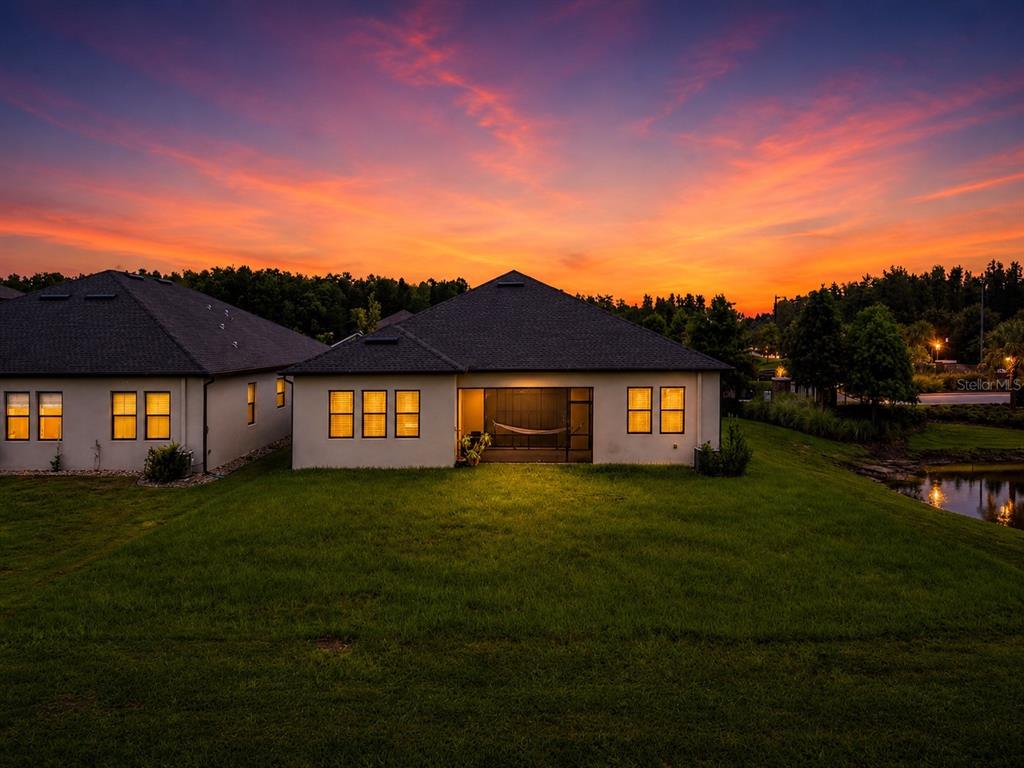 The rear exterior of a single-story house with a screened-in lanai at sunset — 21676 SNOWY ORCHID TERRACE, LAND O LAKES, FL