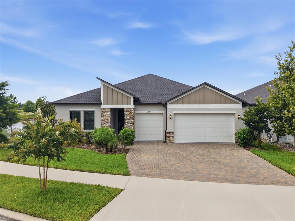 A single-story house with a stone-accented entryway, two garage doors, and a paved driveway — 21676 SNOWY ORCHID TERRACE, LAND O LAKES, FL