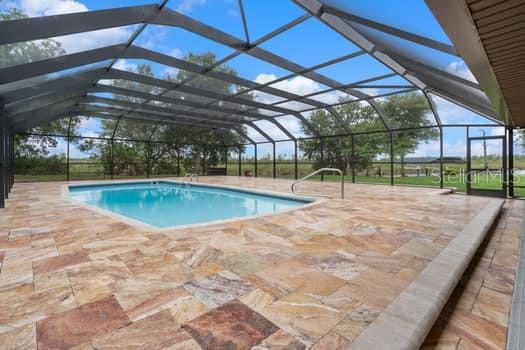 A screened-in pool area with stone pavers and a view of the surrounding landscape — 2309 CYPRESS WALK WAY, RUSKIN, FL