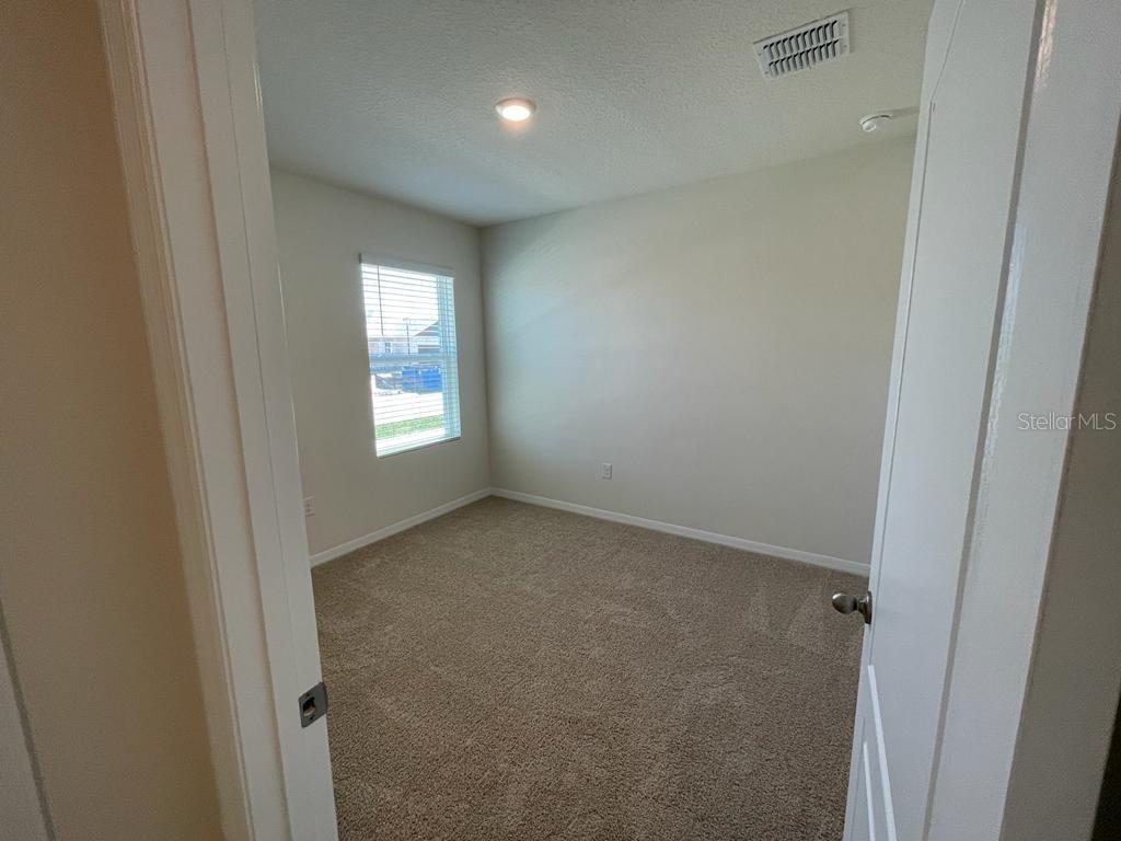 An empty bedroom features beige walls, tan carpeting, a single window, and a ceiling light — 1533 QUINTA ROAD, KISSIMMEE, FL