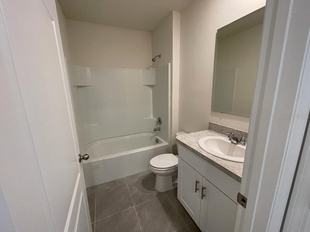 A bathroom features a white tub-shower combo, a vanity with a sink, and tiled flooring — 1533 QUINTA ROAD, KISSIMMEE, FL