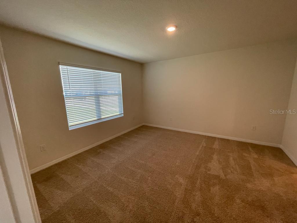 An empty bedroom features beige carpet, light-colored walls, and a window with white blinds — 1533 QUINTA ROAD, KISSIMMEE, FL