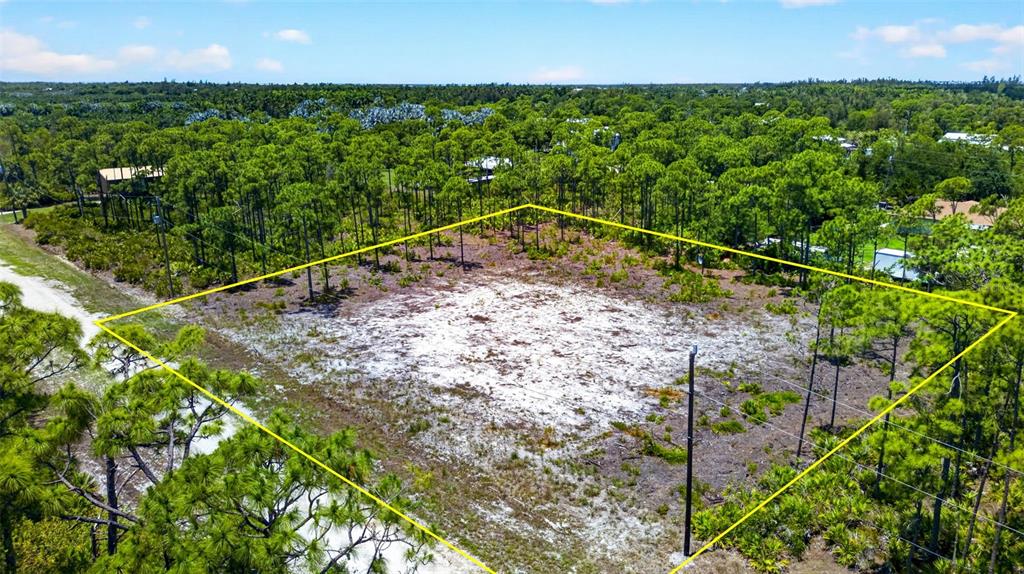 An aerial view shows a rectangular, sandy, undeveloped lot surrounded by pine trees — 15093 MARTINIQUE WAY, BOKEELIA, FL