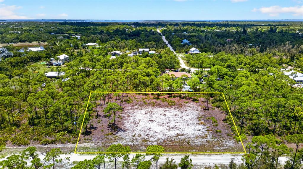 An aerial view shows a rectangular, cleared lot surrounded by dense trees and nearby houses — 15093 MARTINIQUE WAY, BOKEELIA, FL