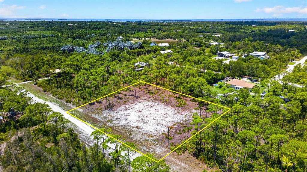 An aerial view shows a rectangular, cleared sandy lot surrounded by dense pine trees — 15093 MARTINIQUE WAY, BOKEELIA, FL