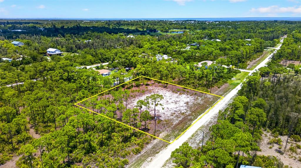 An aerial view shows a cleared, rectangular plot of land surrounded by dense pine forest — 15093 MARTINIQUE WAY, BOKEELIA, FL