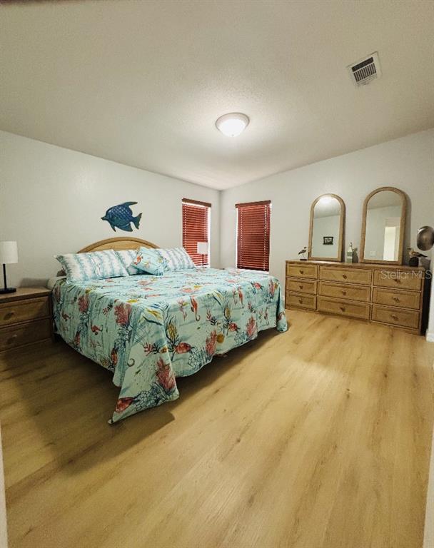 A bedroom features a king bed with a coastal quilt, wood flooring, and a dresser — 6191 TERN DRIVE, ENGLEWOOD, FL