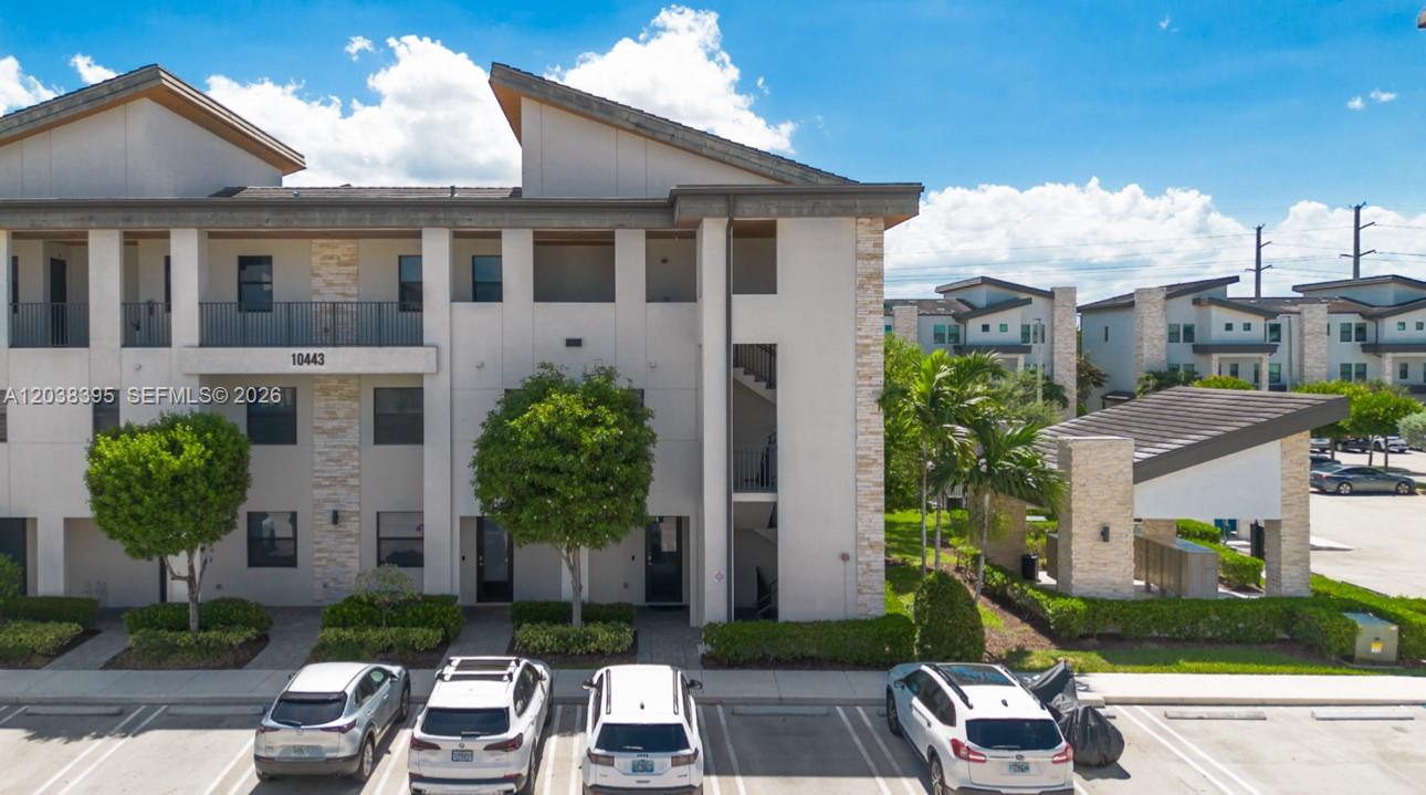 An exterior view of a multi-story apartment building with a parking lot in front — 10443 NW 82nd St # 8, Doral FL 33178, DORAL, FL