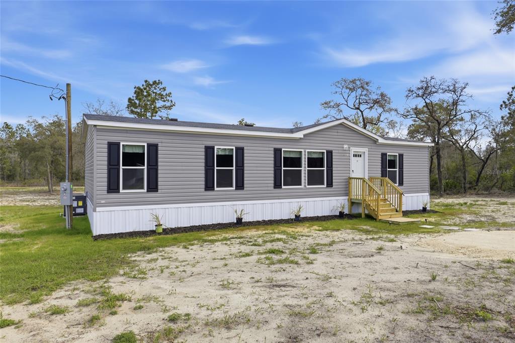 A gray manufactured home with white skirting and a small wooden porch sits on land — 2231 SE 132ND COURT, MORRISTON, FL