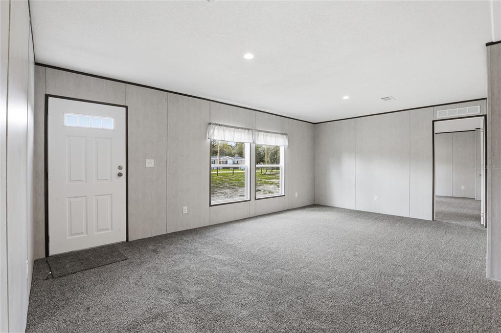 A living room with gray carpet, light wood-paneled walls, a white front door, and windows — 2231 SE 132ND COURT, MORRISTON, FL