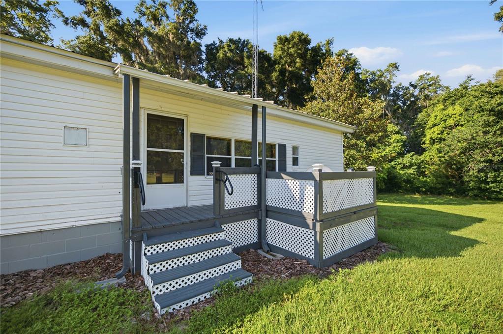 A white mobile home features a small wooden deck with lattice railings and stairs — 4950 SE 112TH STREET ROAD, BELLEVIEW, FL