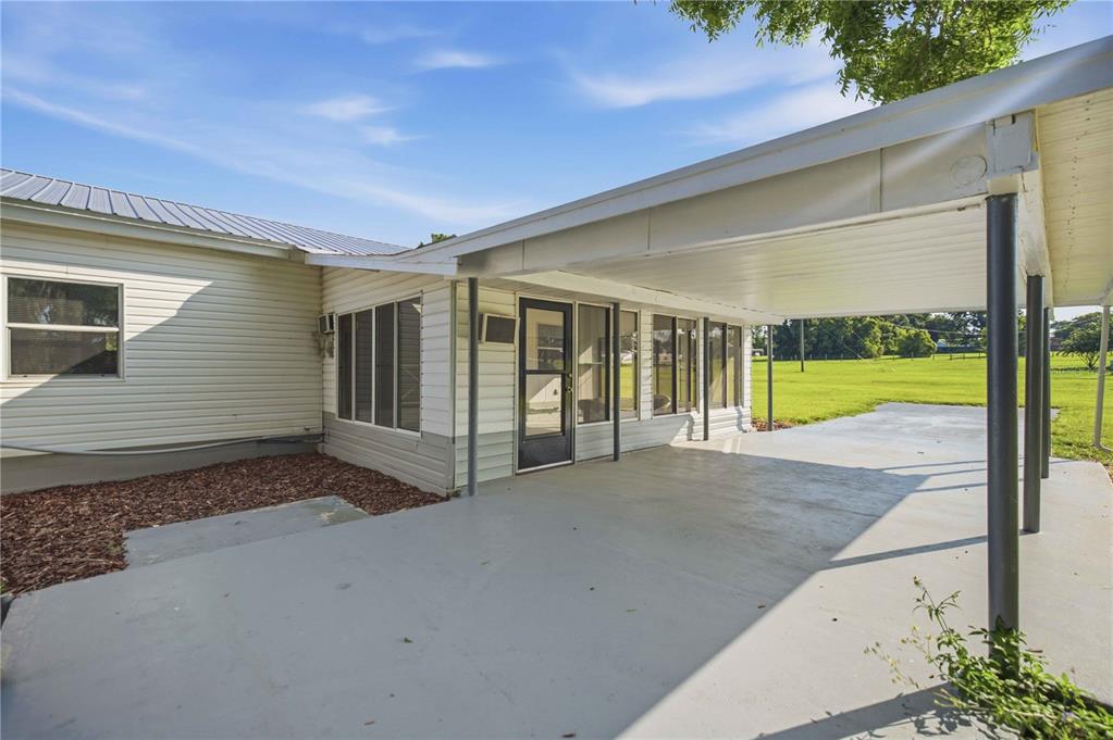 A covered concrete patio sits adjacent to a house with white siding and large windows — 4950 SE 112TH STREET ROAD, BELLEVIEW, FL