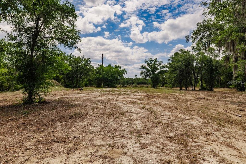 A cleared, sandy lot is surrounded by trees under a cloudy blue sky — 2271 ASPEN ROAD, PUNTA GORDA, FL