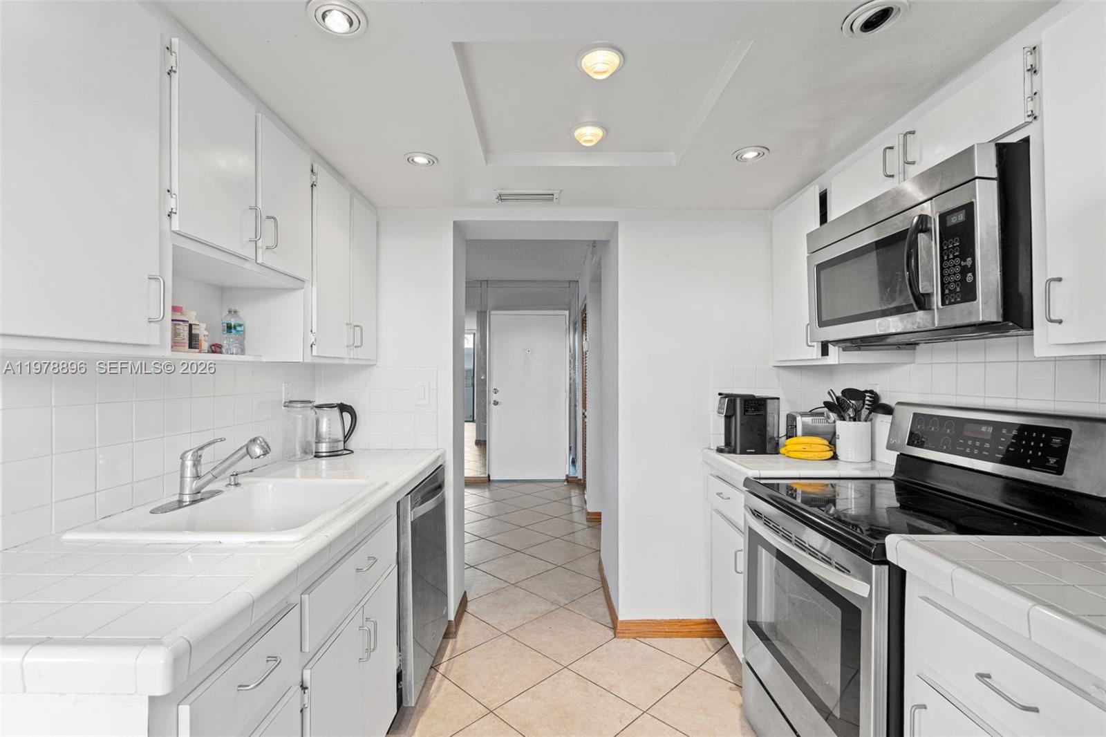 A galley kitchen features white cabinets, tiled countertops, stainless steel appliances, and tile flooring — 7300 Wayne Ave # 217, Miami Beach FL 33141, MIAMI BEACH, FL