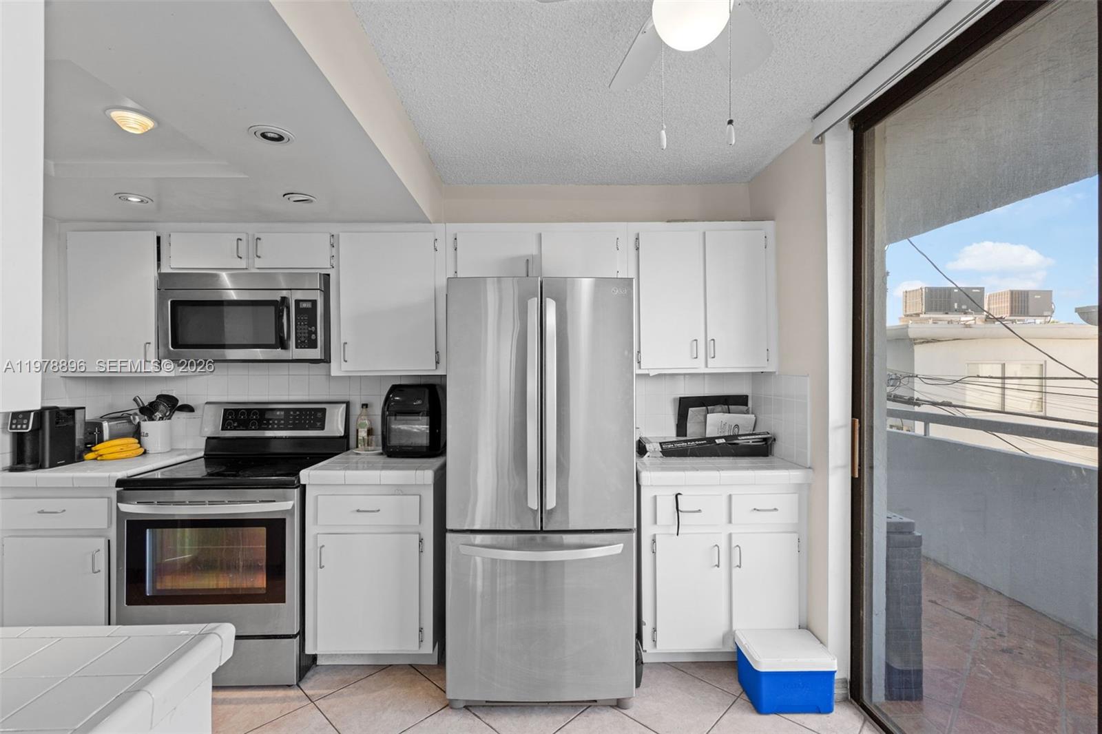 A kitchen features white cabinets, stainless steel appliances, tile countertops, and a sliding glass door — 7300 Wayne Ave # 217, Miami Beach FL 33141, MIAMI BEACH, FL