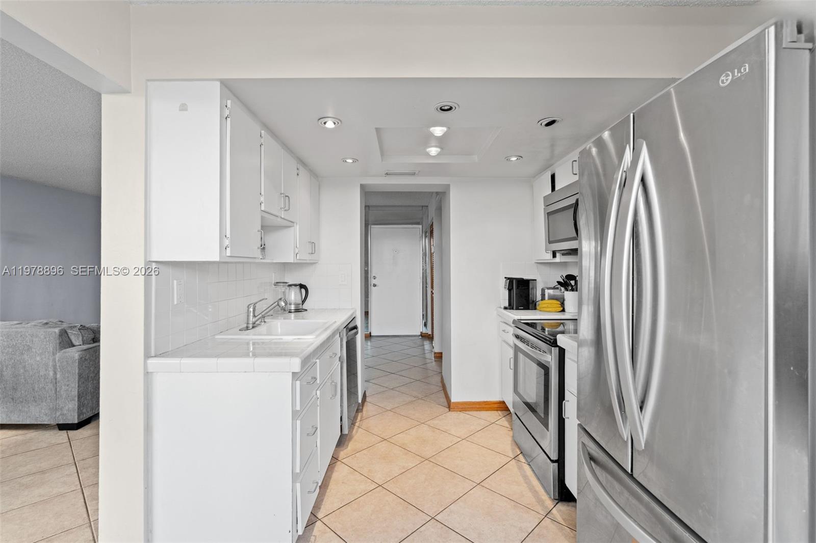 A galley kitchen features white cabinets, tile countertops, and stainless steel appliances — 7300 Wayne Ave # 217, Miami Beach FL 33141, MIAMI BEACH, FL