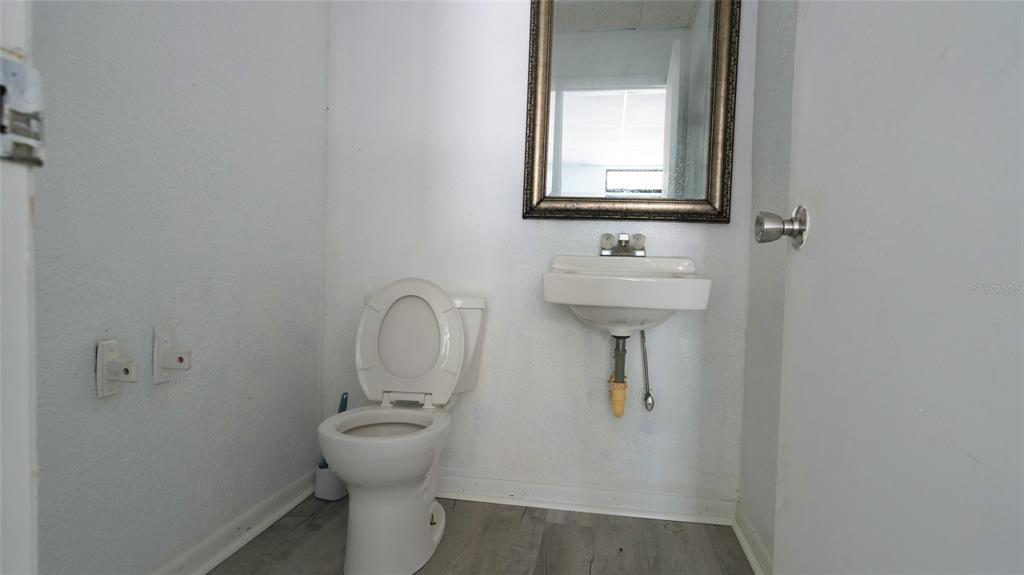 A small bathroom features a white toilet, a wall-mounted sink, and a framed mirror — 5650 PARK BOULEVARD N UNIT 6, PINELLAS PARK, FL