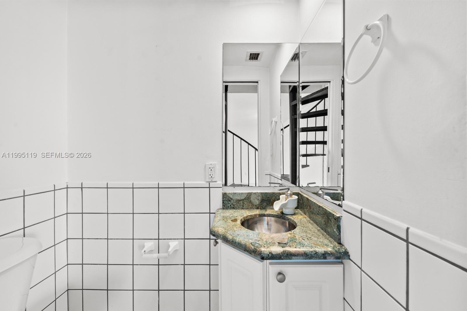 A small bathroom features white tiled walls, a corner vanity with a stone countertop, and a mirror — 2987 Bird Ave, Miami FL 33133, MIAMI, FL