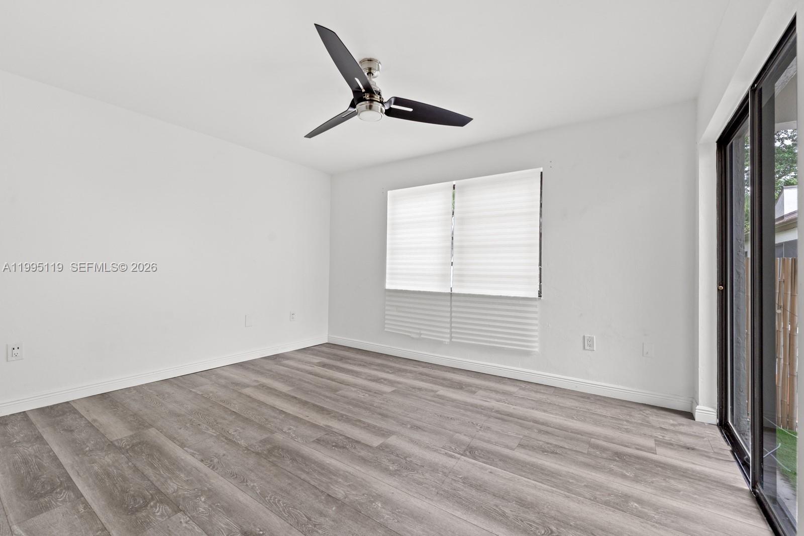 An empty room features white walls, gray wood-look flooring, a ceiling fan, and sliding doors — 2987 Bird Ave, Miami FL 33133, MIAMI, FL