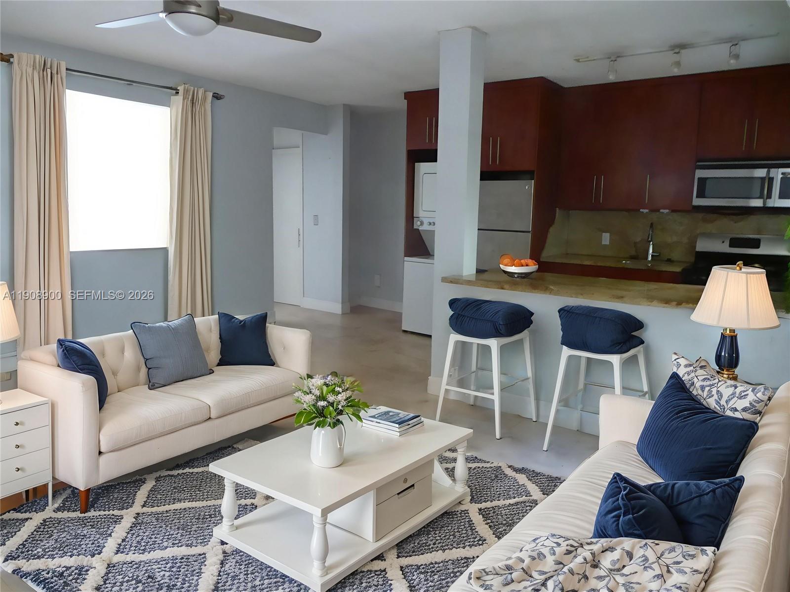A living room with a white sofa, coffee table, and an open kitchen with bar stools — 101 Collins Ave # 2, Miami Beach FL 33139, MIAMI BEACH, FL